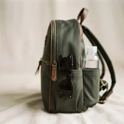 Side view of the mini backpack highlighting the two exterior slip pockets holding sunglasses and a small water bottle.