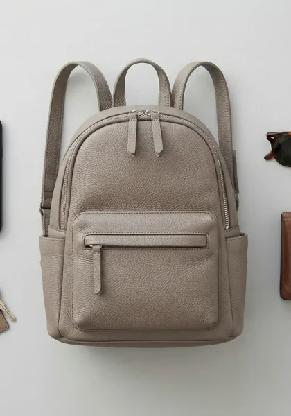 A flat lay arrangement of the Stone & Co. mini backpack with common daily items like a phone, keys, wallet, and sunglasses laid out next to it.